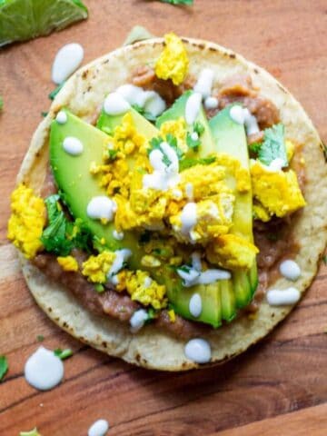 Vegan Breakfast Tostadas with Tofu Scramble, Avocado and Beans on a wood countertop with vegan cashew cream drizzled on top.