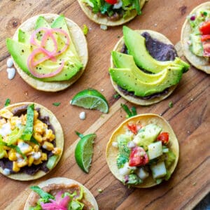 assorted mini tostadas topped with various vegan, meatless, vegetarian toppings of beans, ceviche, corn, crema, pickled onion, avocado and lettuce