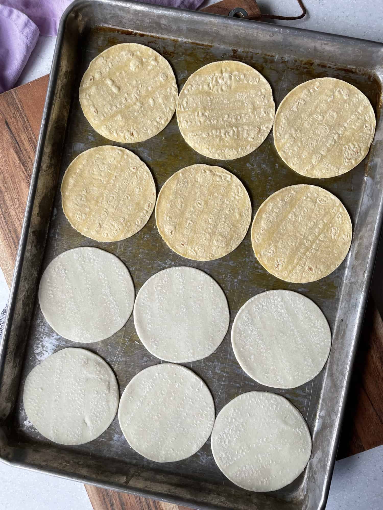 12 street taco corn tortillas spread out on baking sheet in since layer (six white and six yellow)
