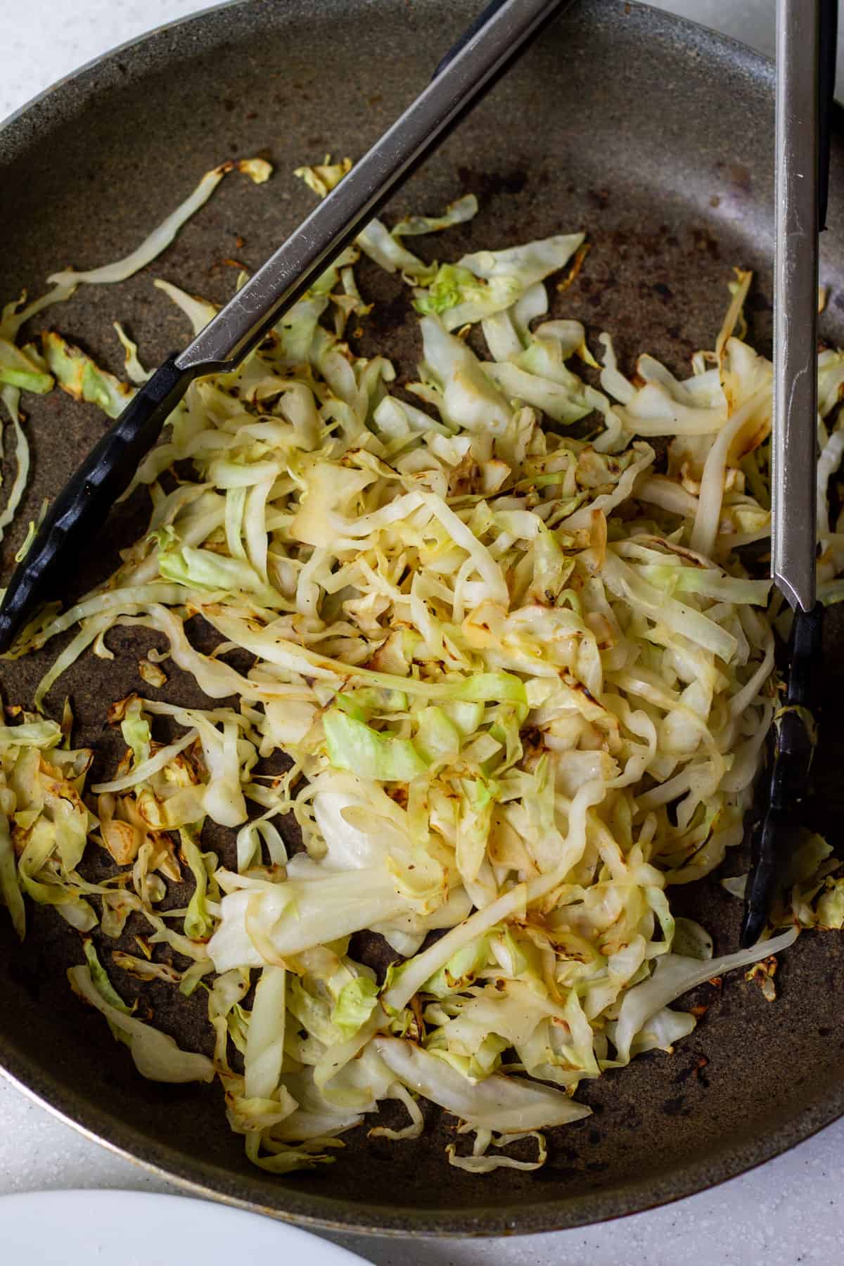 pan-seared green cabbage strips charred in a skillet on the stove, with tongs