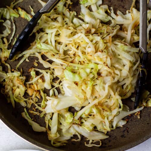 pan-seared green cabbage strips charred in a skillet on the stove, with tongs