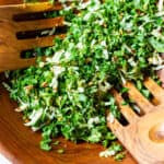 wooden salad bowl of kale cabbage salad with wooden salad forks tossing it