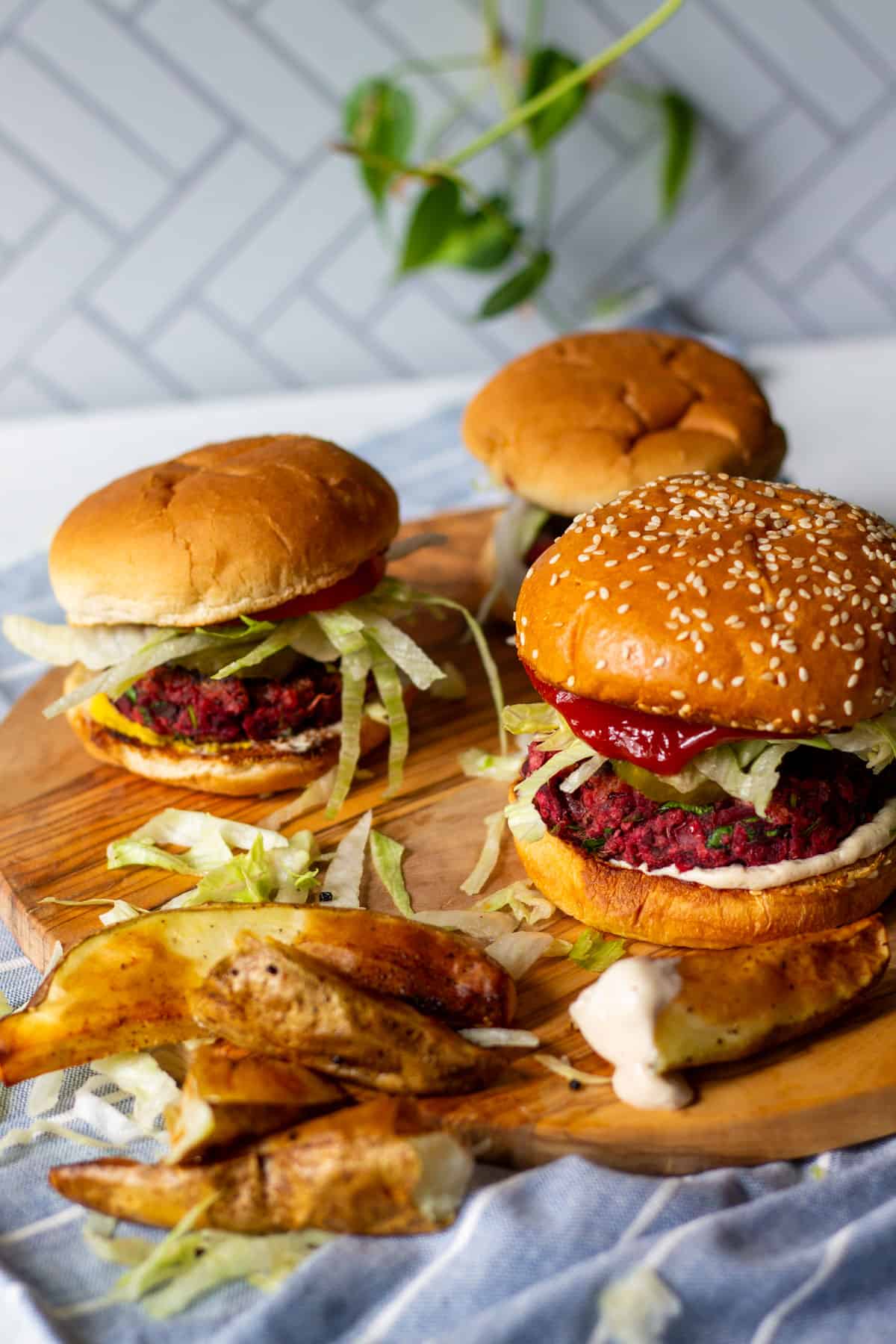 three beet burgers on wooden board and potato wedges in front