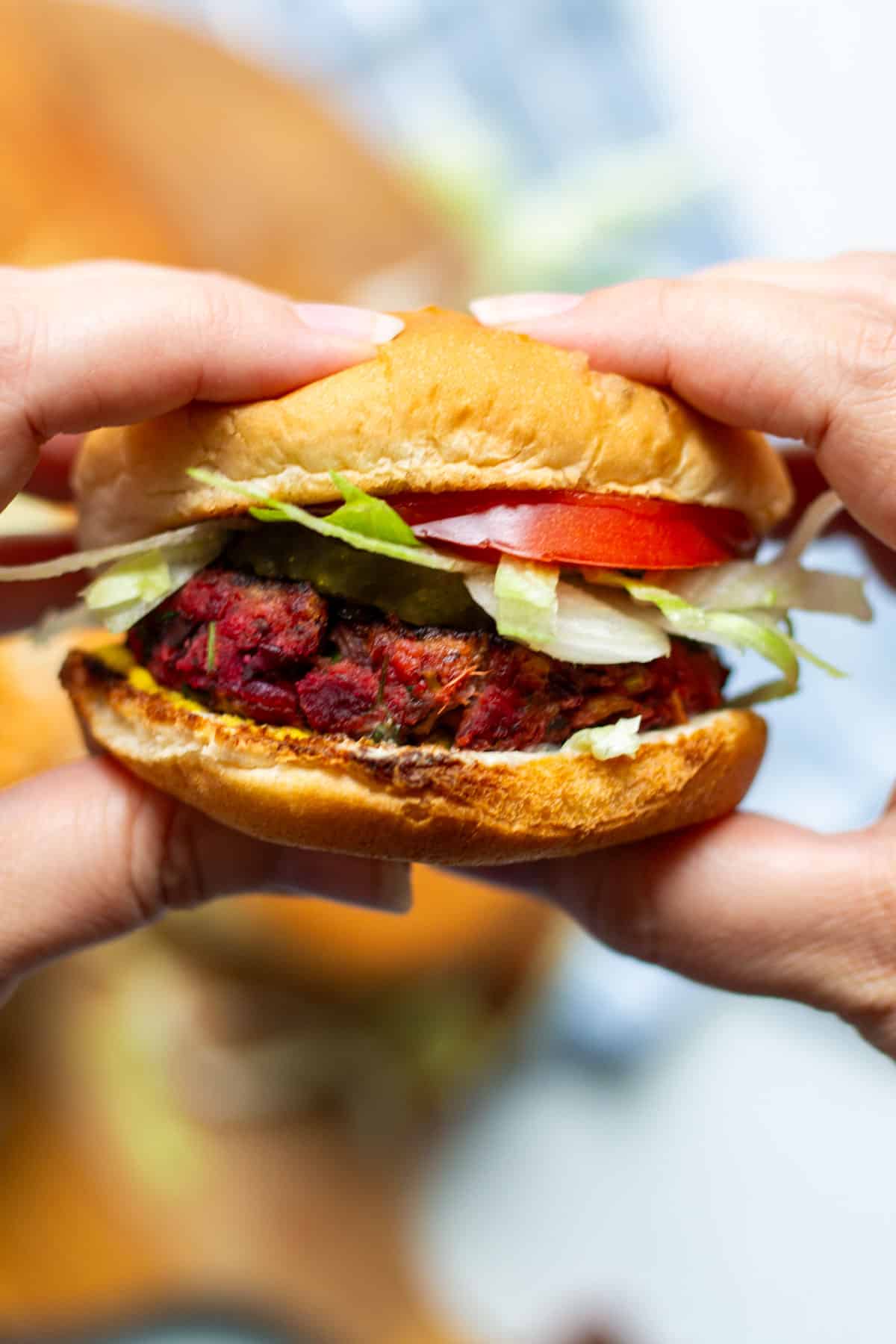 holding a vegan beet slider burger with ketchup, mayo, lettuce, pickled and tomato