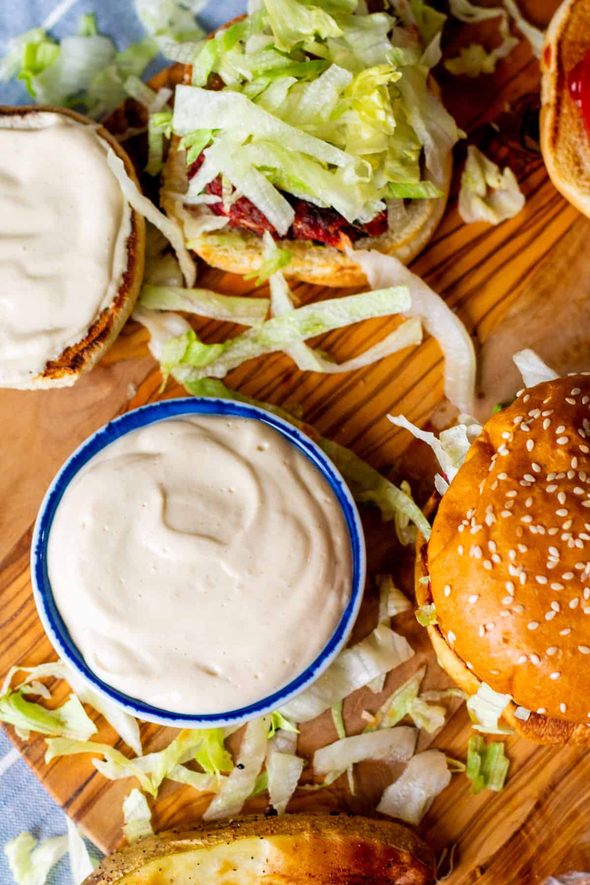 veggie burgers with vegan cashew tofu mayo spread on buns and in bowl over wooden board