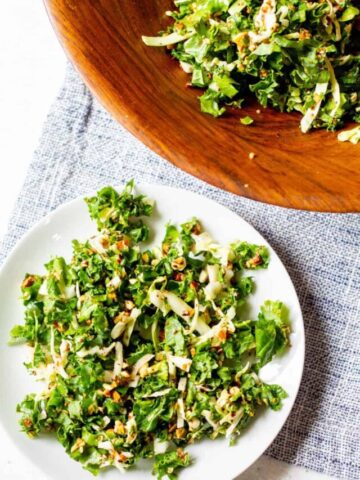 kale cabbage salad with roasted almonds on a plate with more in a wooden bowl on the side