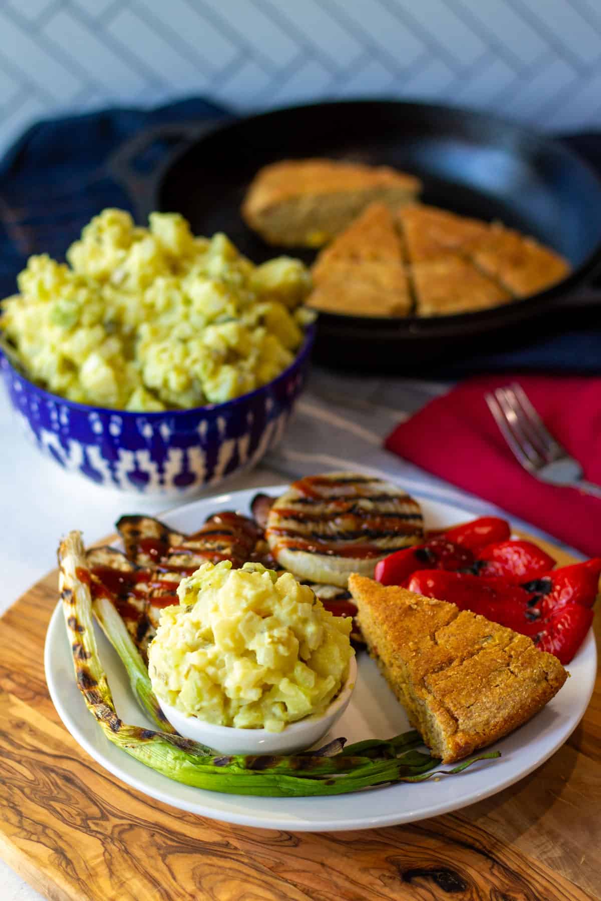 White plate with potato salad, grilled eggplant, grilled onion and cornbread