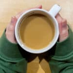 hands holding a mug of hot creamy black tea