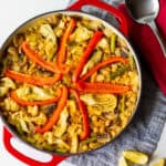 pan of cooked vegetable paella with red bell peppers in a starburst pattern on top. Lemon wedges and spoon on side.