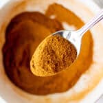 small spoonful of mixed pumpkin pie spice hovering over a small bowl