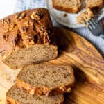 slices of banana nut bread on a cutting board with a plate of banana bread in the background