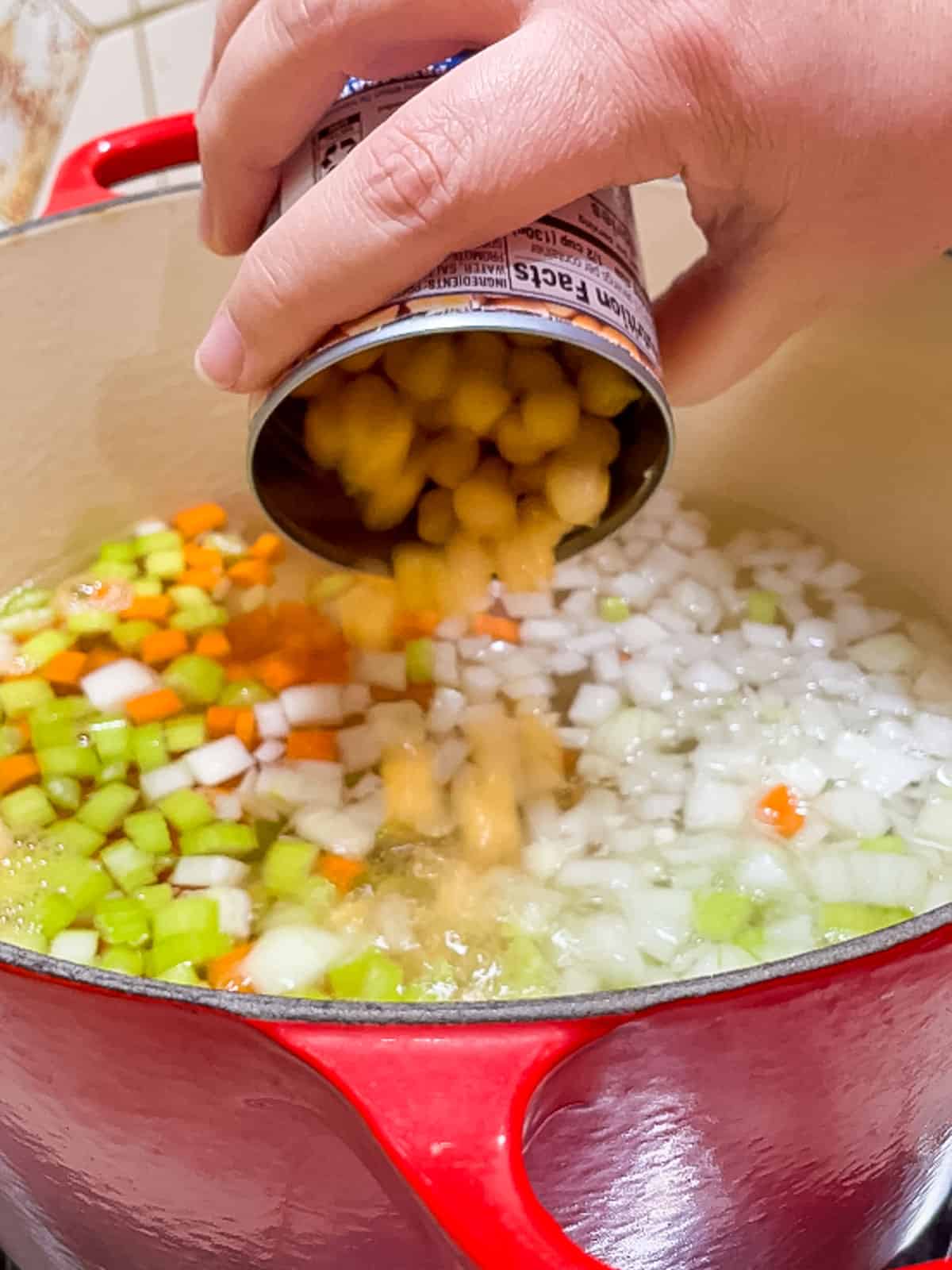 pouring chickpeas into soup pot, where onion, celery and carrots are