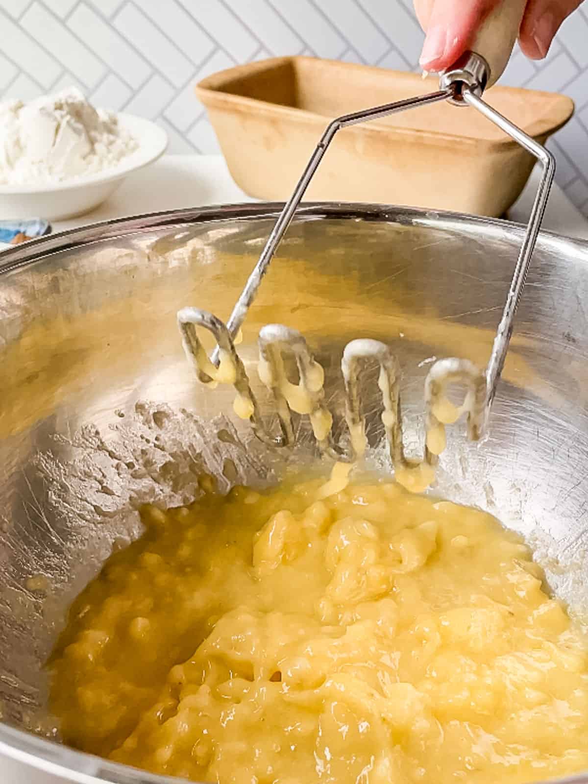 mashing bananas with potato masher in metal bowl