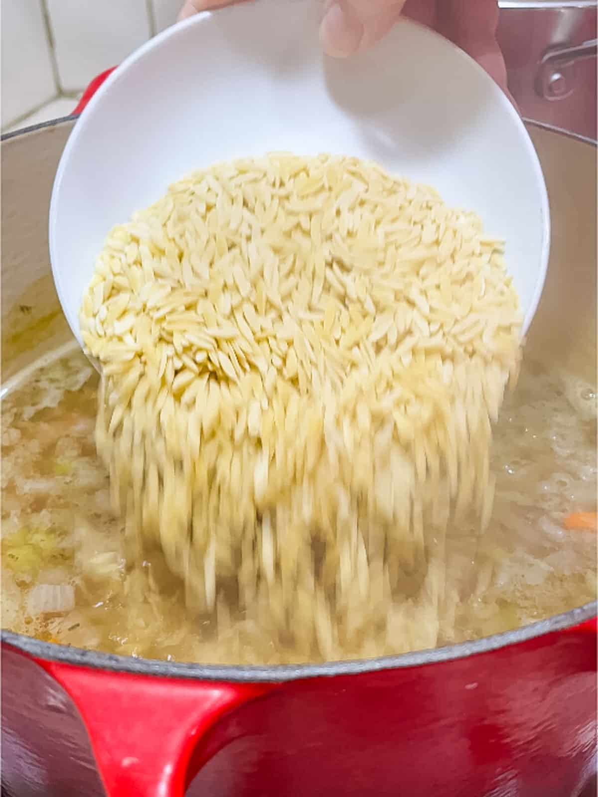 pouring orzo into soup pot