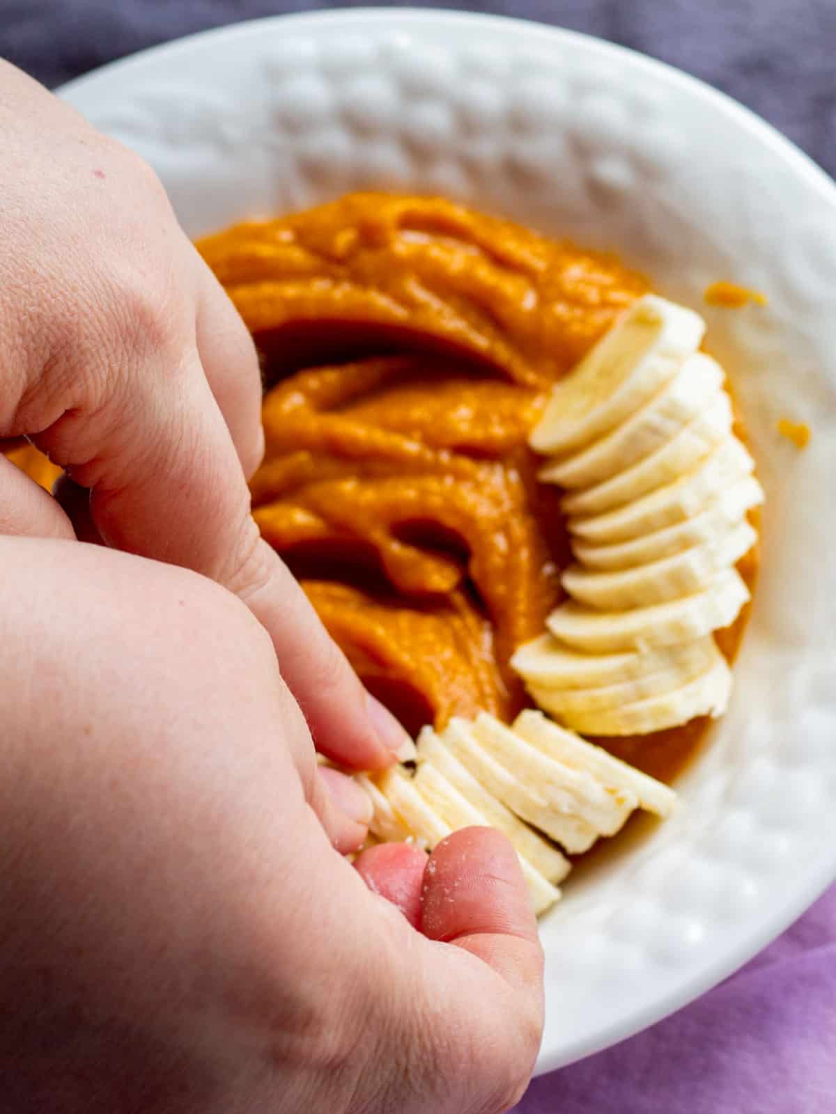 topping sweet potato pudding in a white bowl with sliced banana on the side