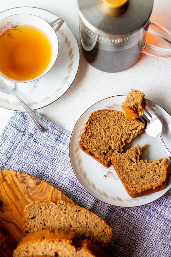 cut slice of banana bread on a plate with light tea in a tea cup