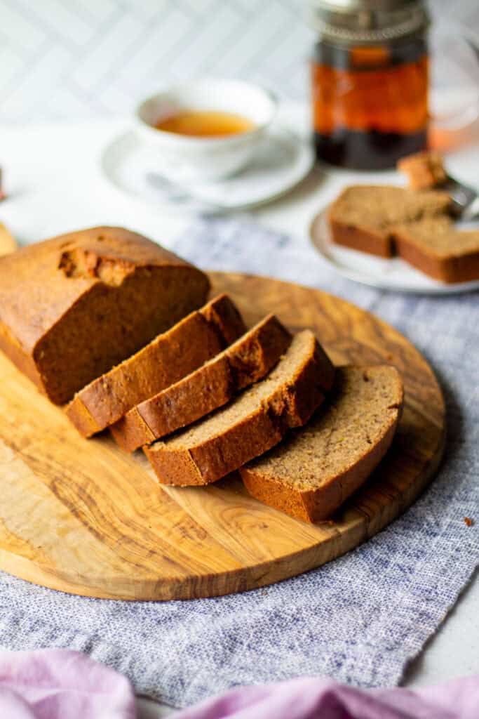 sliced loaf of banana bread on cutting board with tea in background