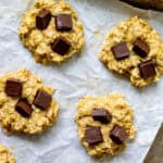 four banana oatmeal cookies with chocolate chunks on a parchment-paper lined baking tray