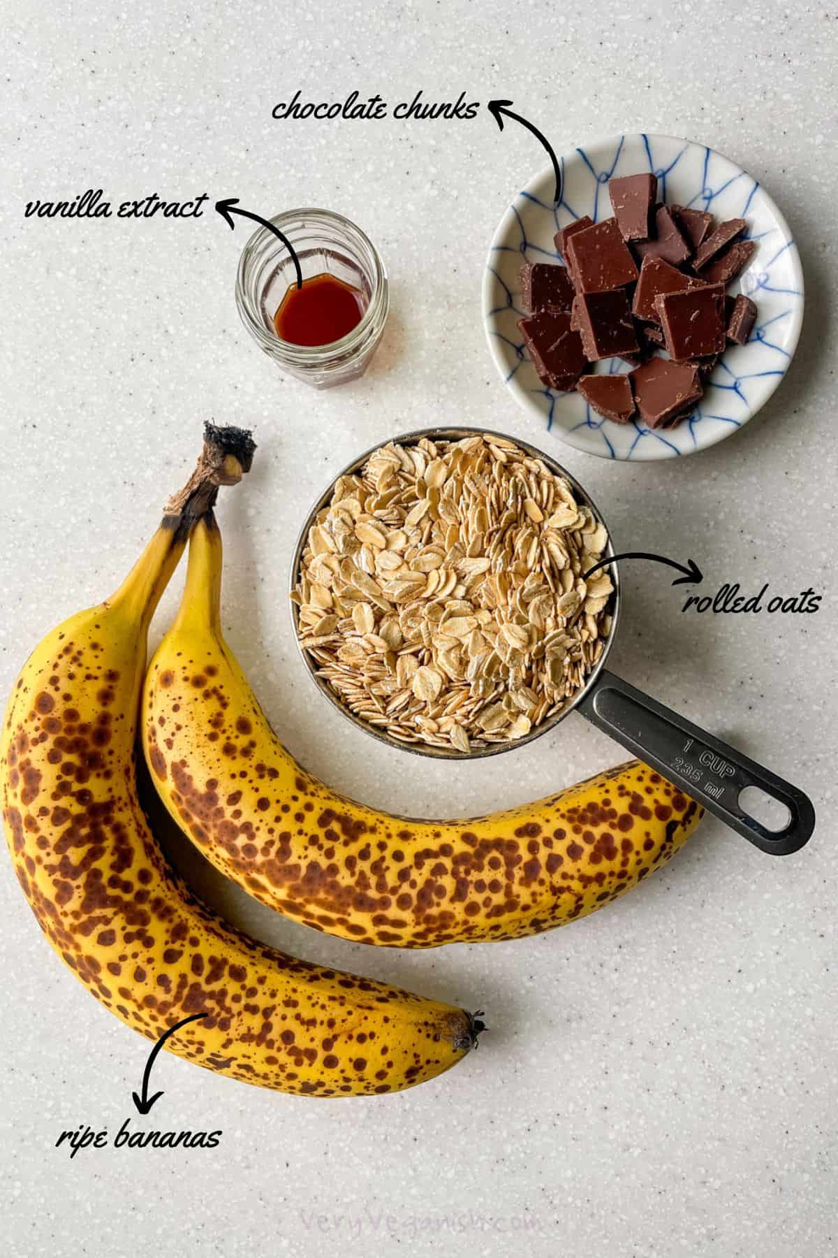 Ingredients for banana oat chocolate chunk cookies on counter (ripe bananas, oats, chocolate chunks and vanilla extract)