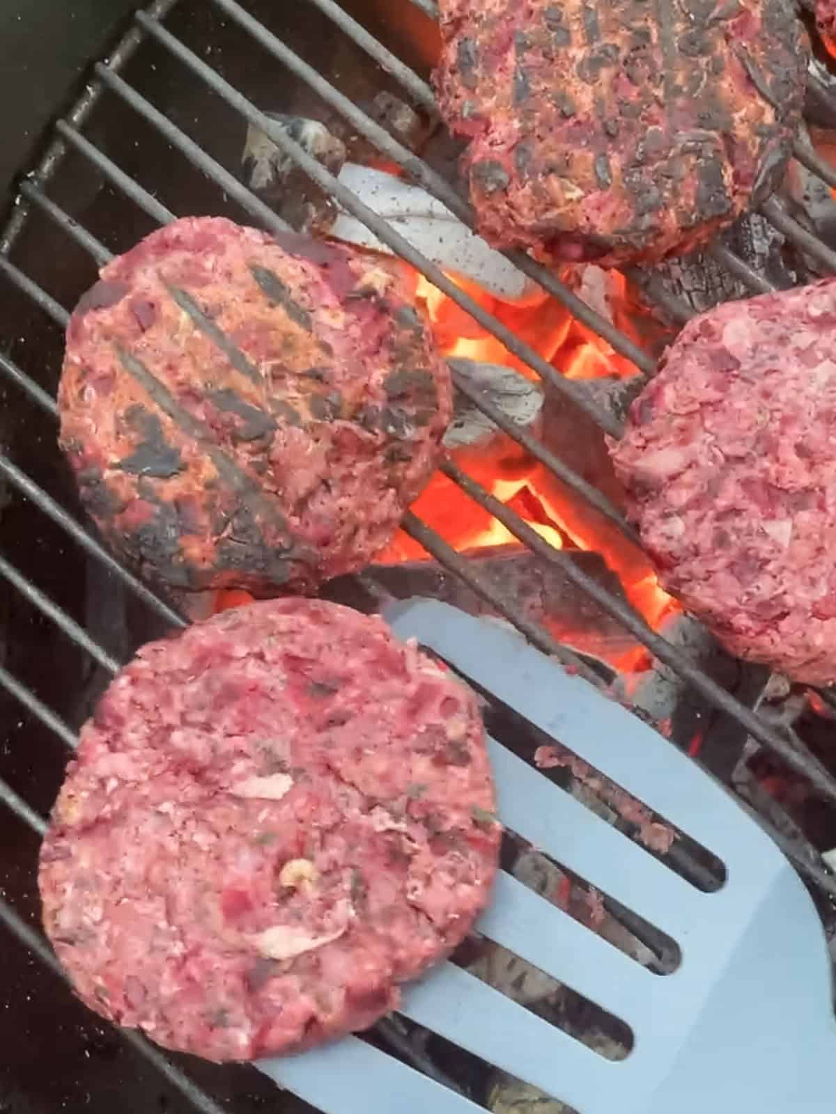 Flipping grilled kidney bean burgers on weber grill over fire