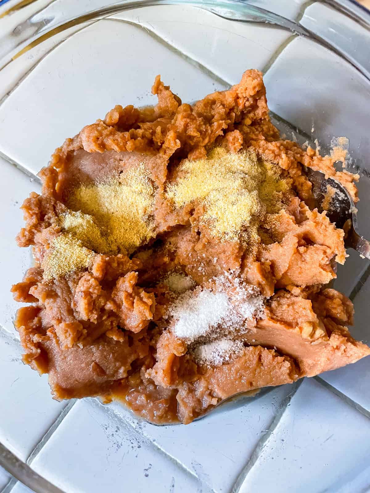glass bowl with refried beans, spices and water unmixed at the bottom of the bowl