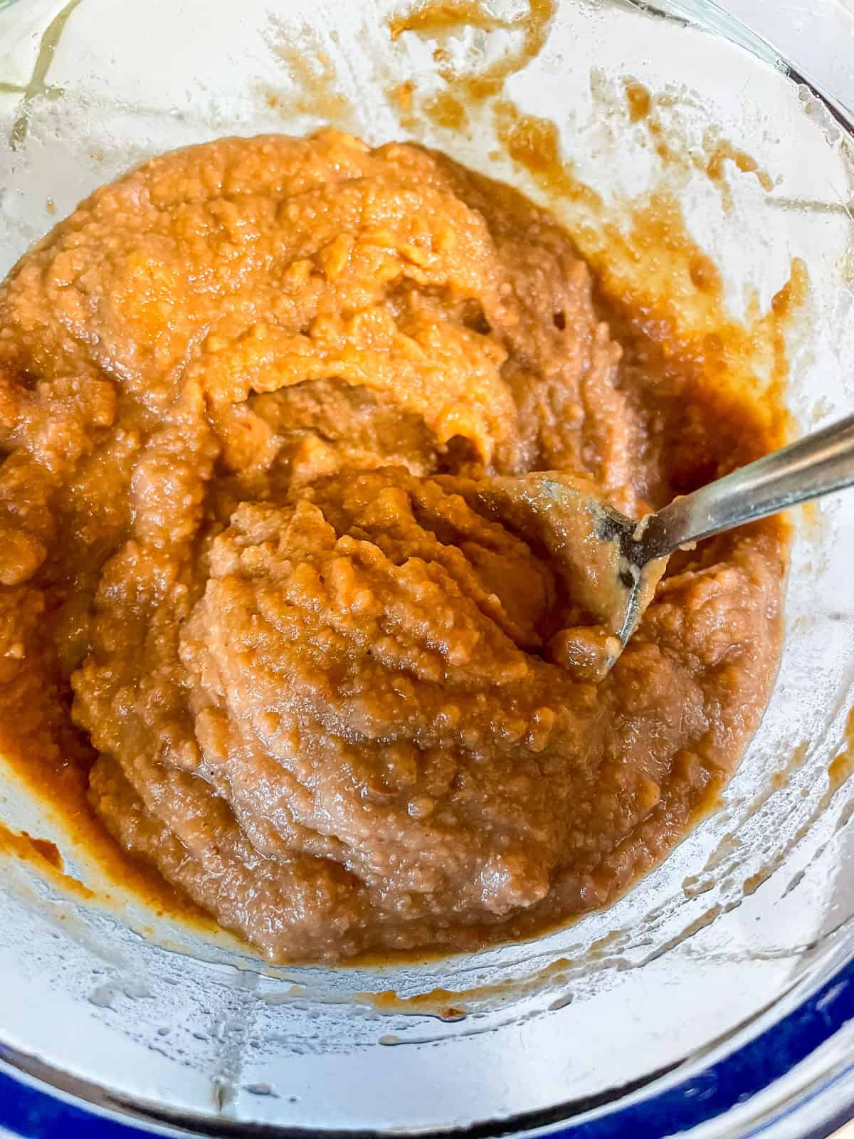 Mixed and seasoned refried beans in a glass bowl being stirred with a spoon, before heating up in the microwave