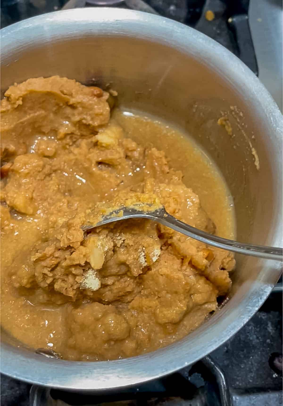 Stirring spices and water into the refried beans in a stainless steel pan on the stove