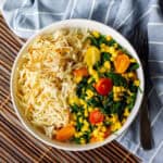 white bowl with air fryer hash browns and veggies in it, with a fork beside the bowl resting on a blue and white striped towel