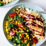 light blue bowl with golden hash browns and cooked spinach, corn and tomato on the side with BBQ sauce drizzled on top and fork in the bowl