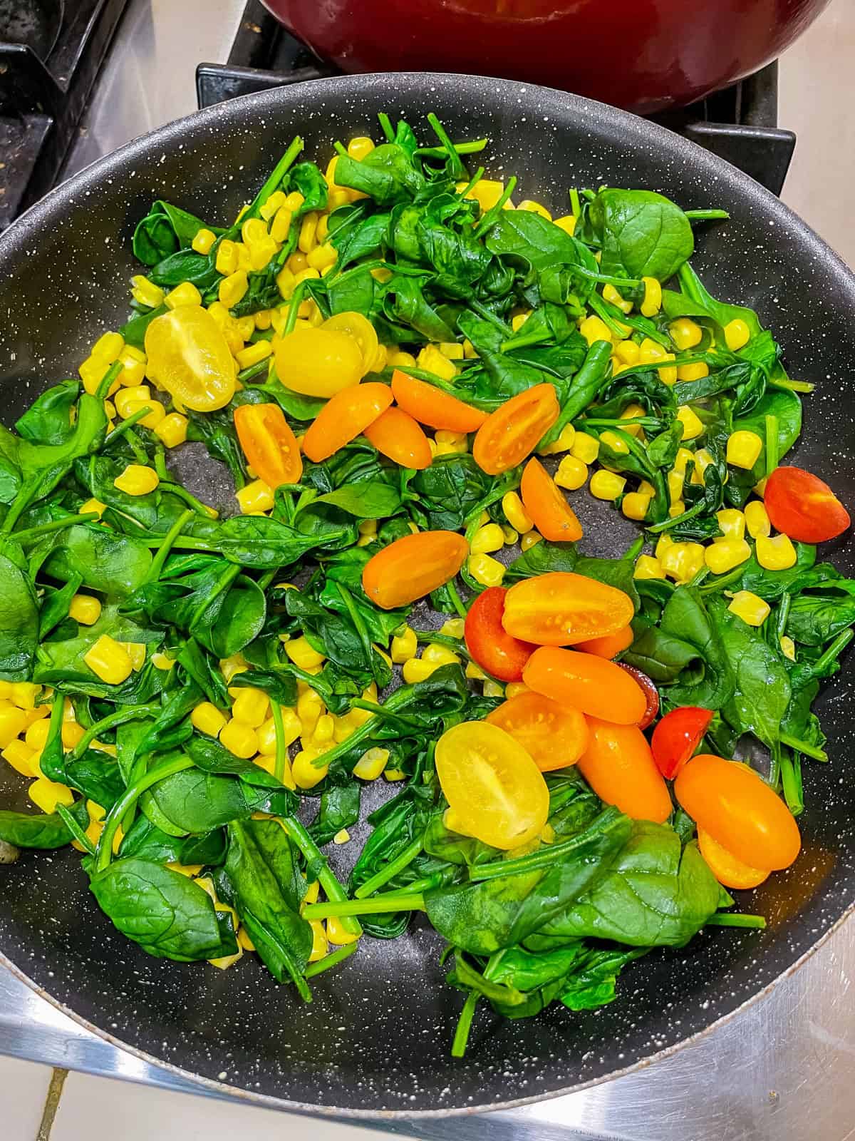 Skillet with wilted spinach, corn and halved cherry tomatoes