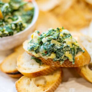 creamy vegan spinach artichoke dip on little pieces of toasted french bread