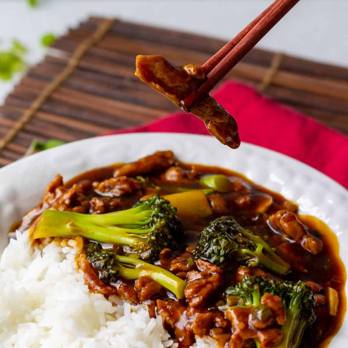 using chopsticks to pick up a piece of soy curl out of white bowl with steamed jasmine rice and soy curl beef and broccoli