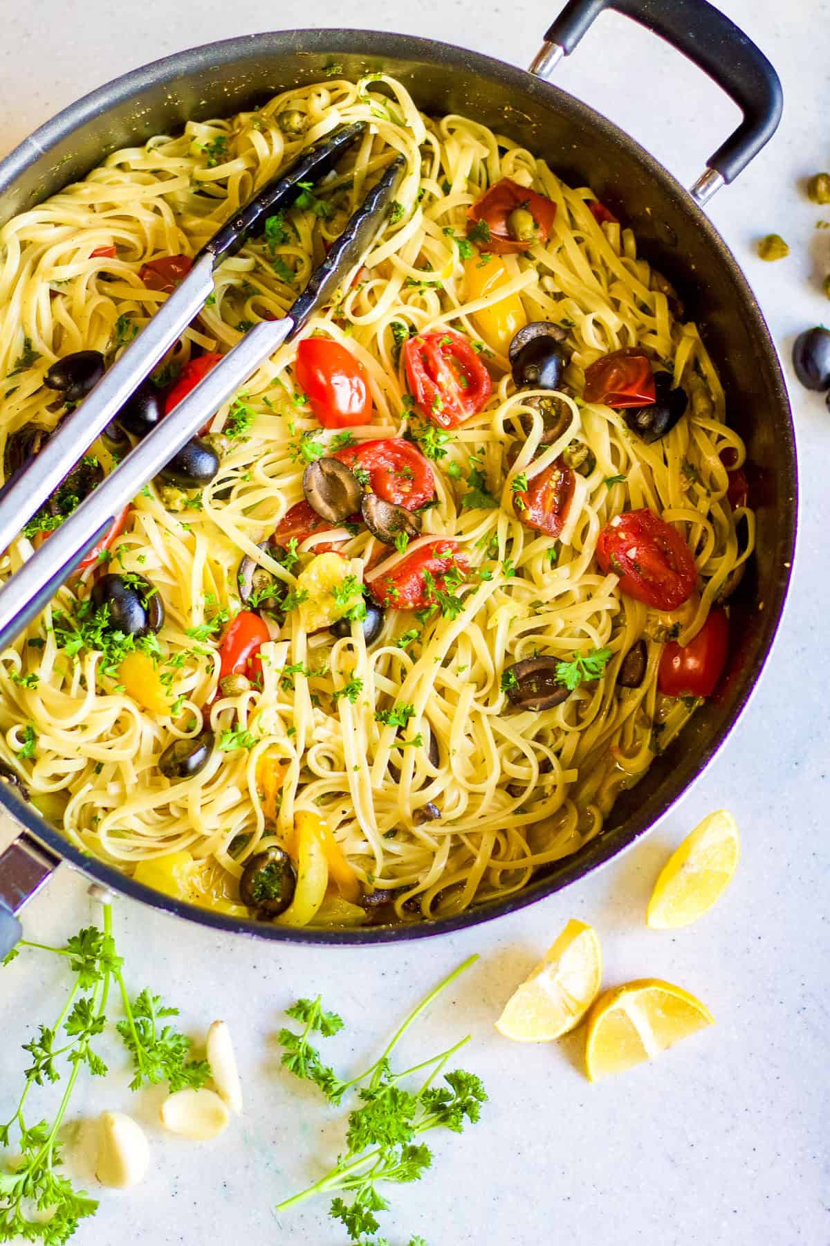 large non-stick skillet with pasta puttanesca and a set of tongs resting inside