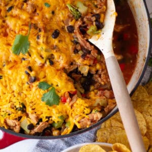 Scooping the cheesy soy curl, black bean, corn and broccoli taco mixture from a wide skillet with tortilla chips on the table near a bowl