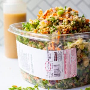 Packed over the top grain and celery copycat Costco salad recipe in a Kirkland plastic container with homemade apple cider vinaigrette dressing in background