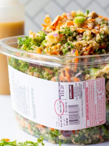 Packed over the top grain and celery copycat Costco salad recipe in a Kirkland plastic container with homemade apple cider vinaigrette dressing in background