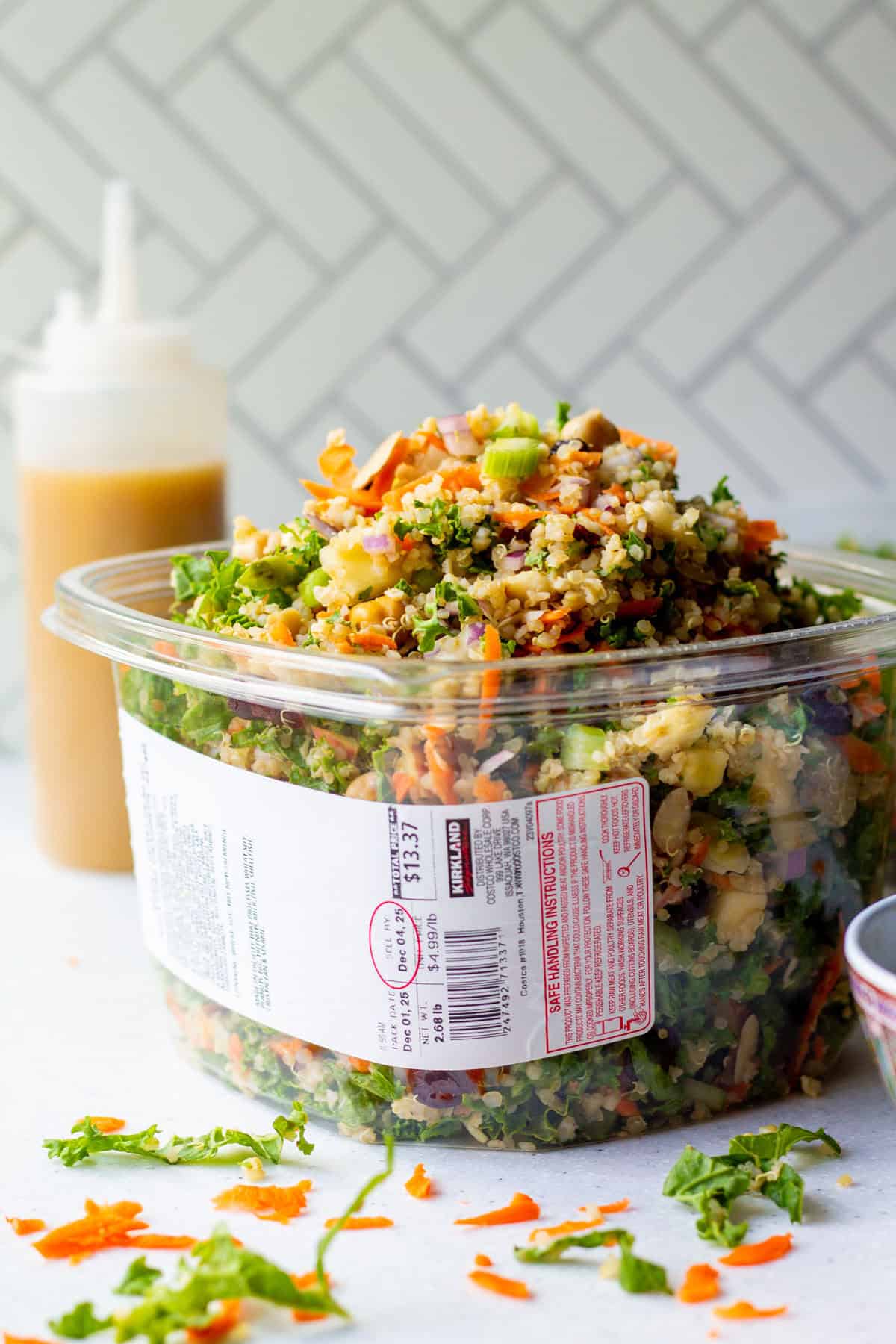 Packed over the top grain and celery copycat Costco salad recipe in a Kirkland plastic container with homemade apple cider vinaigrette dressing in background