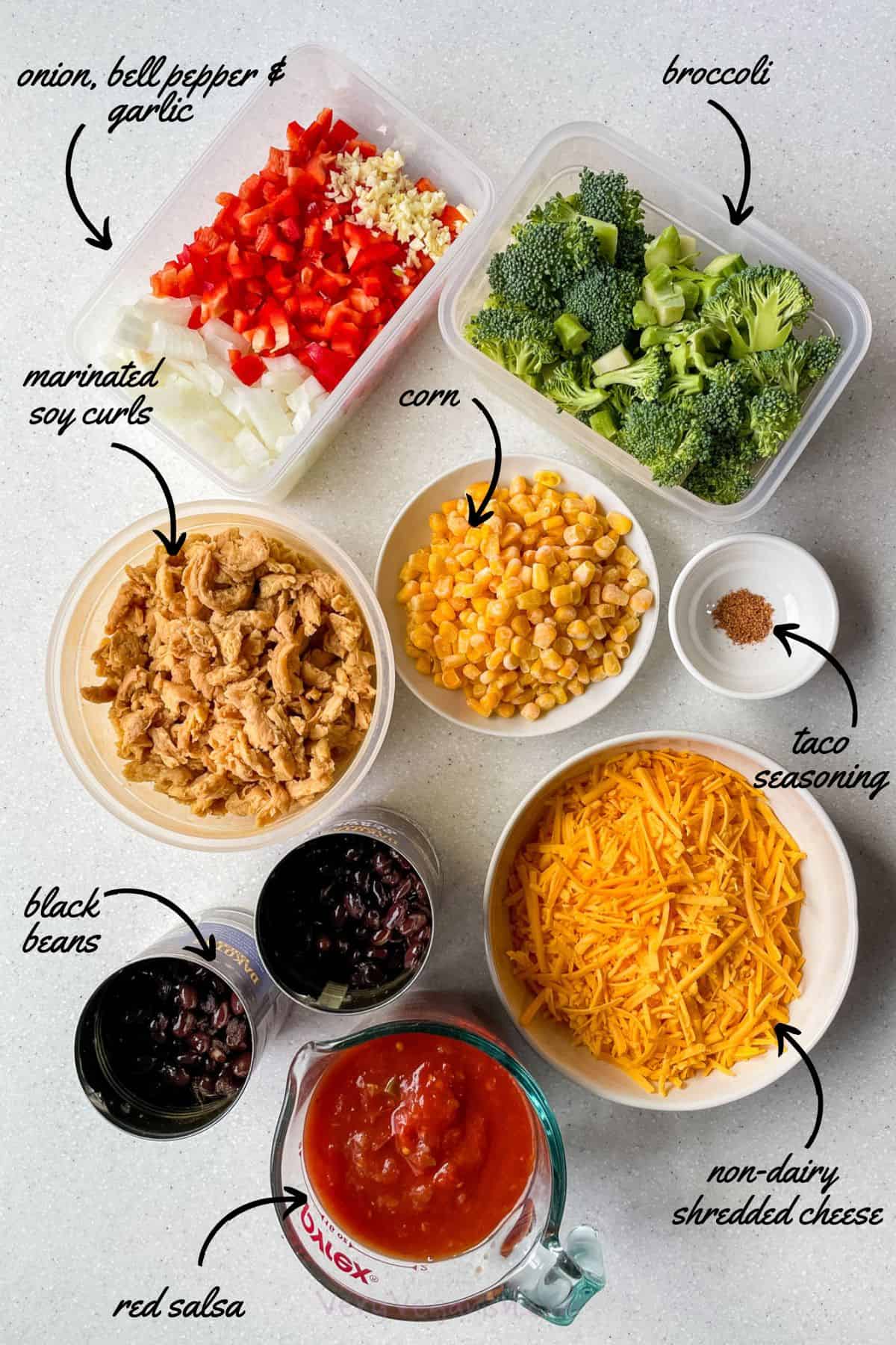 Ingredients laid on table (onion, bell pepper, garlic, broccoli, soy curls, corn, shredded non-dairy cheese, taco seasoning, black beans and salsa) that you need to make this Cheesy Soy Curl Black Bean Taco Skillet Recipe