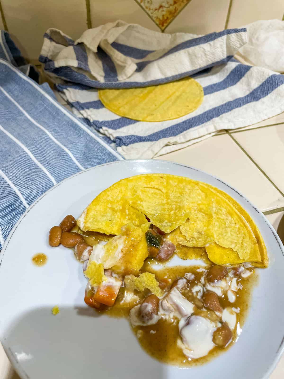 Corn tortilla (heated in dry non-stick pan) filled with beans and sour cream on white plate with more tortillas in tea towel