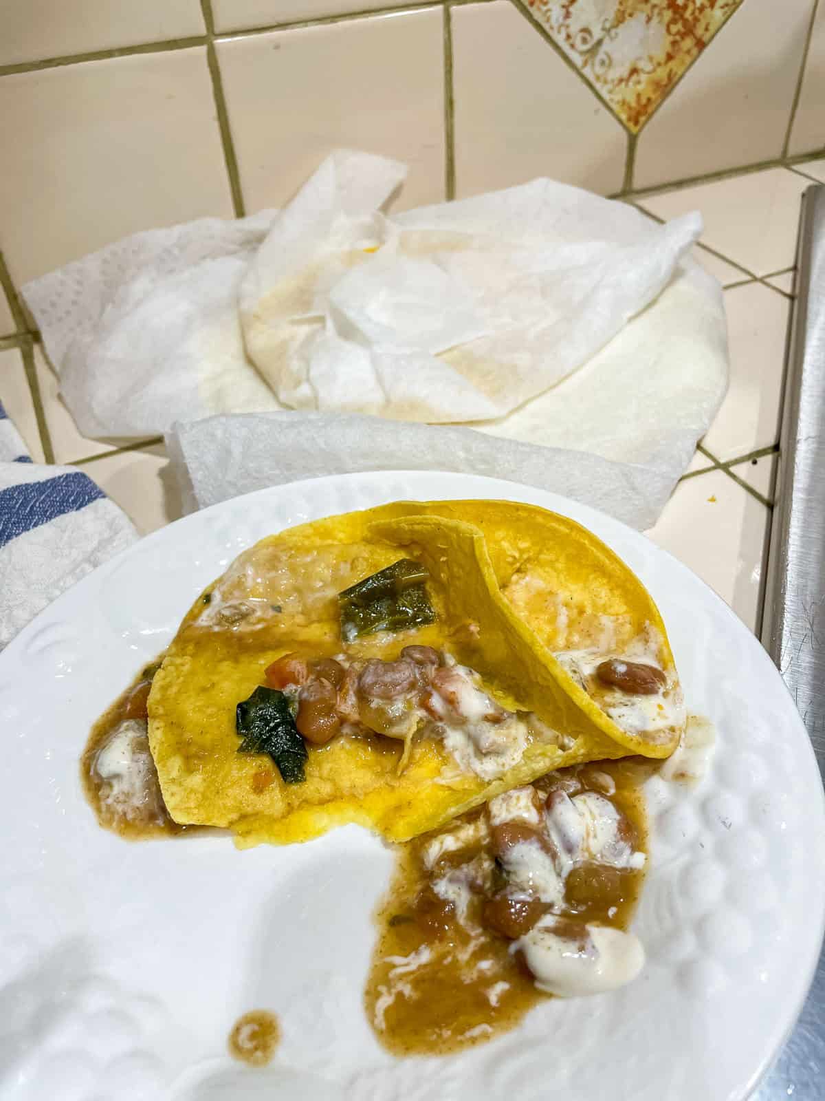 Corn tortilla (heated in microwave inside damp paper towel) filled with beans and sour cream on white plate with more tortillas in tea towel