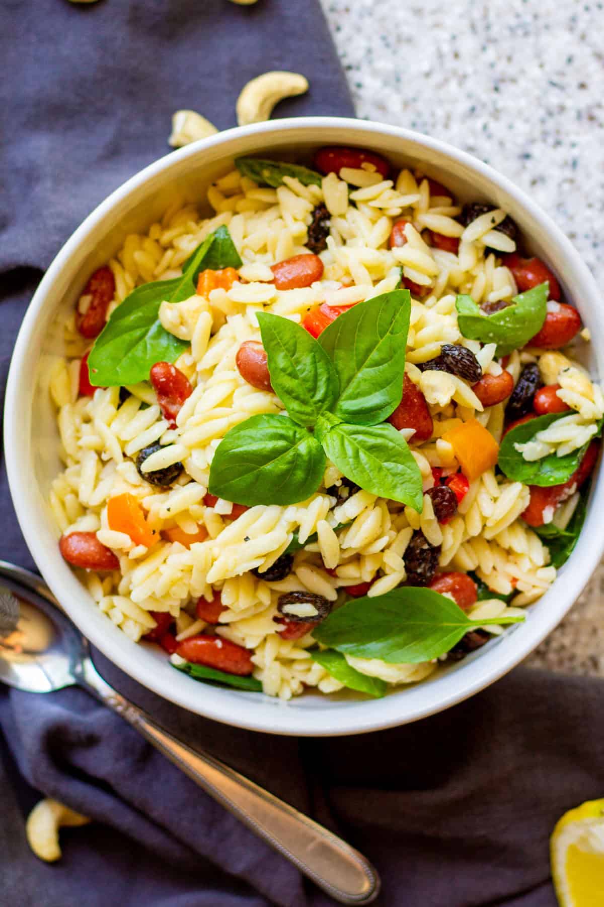 white bowl filled with orzo basil kidney bean vegetable pasta salad with a sprig of fresh basil resting on top and a spoon nearby