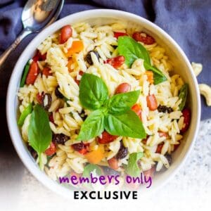 white bowl filled with orzo basil kidney bean vegetable pasta salad with a sprig of fresh basil resting on top and a spoon nearby
