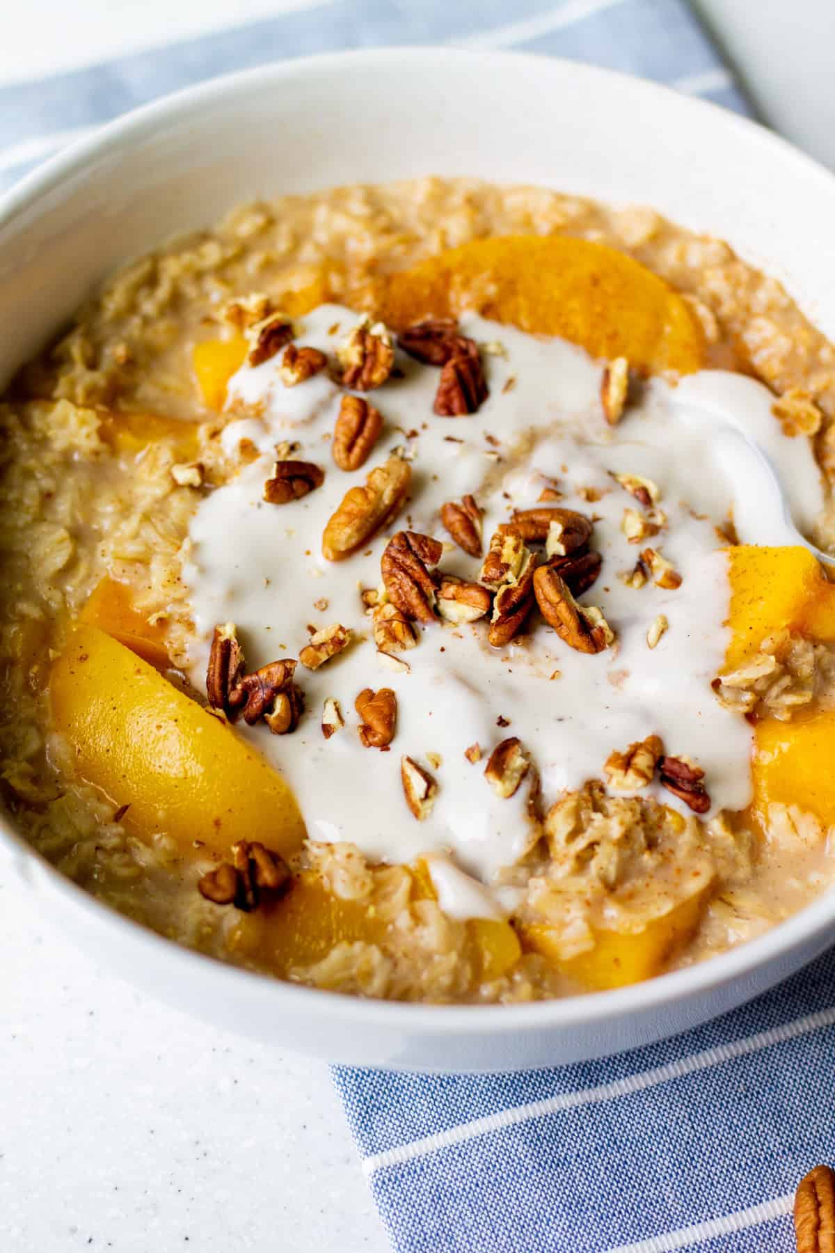 white bowl full of non-dairy peaches and cream oatmeal with pecans and vanilla yogurt on top
