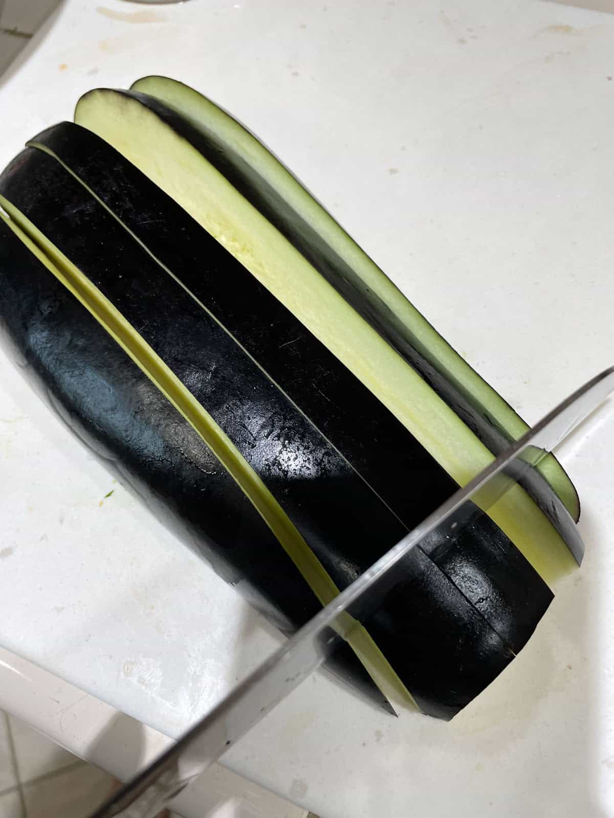 eggplant sliced lengthwise on cutting board and large knife cutting it to make cubes