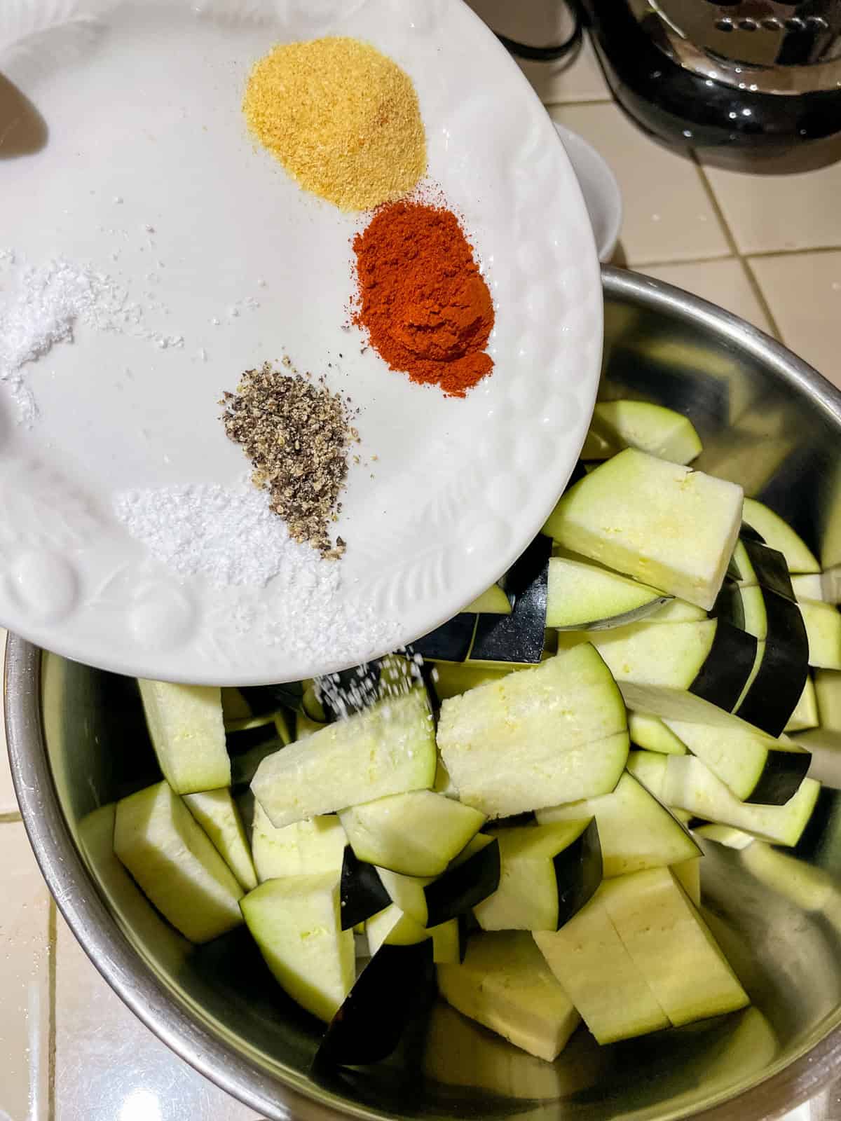 spices, measured out on small plate, being poured into mixing bowl, where eggplant and onions are