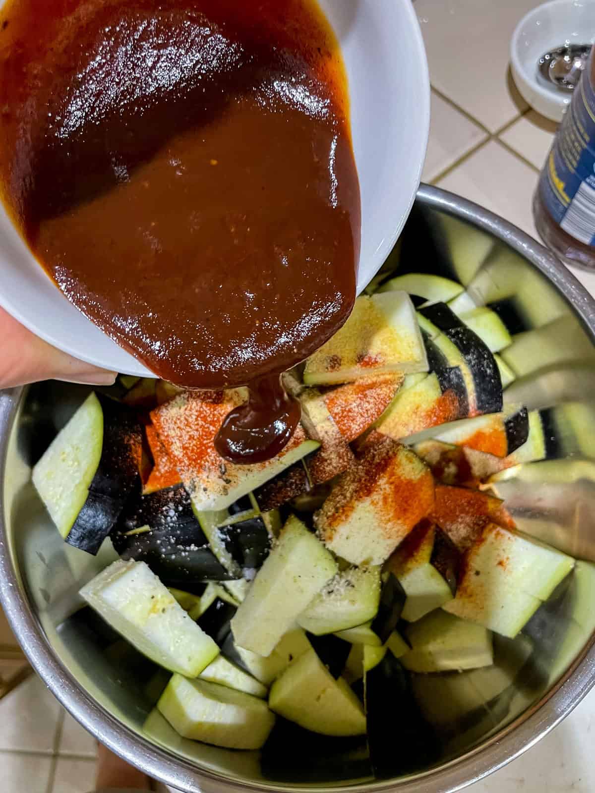 pouring BBQ sauce into mixing bowl over eggplant, onion and spices
