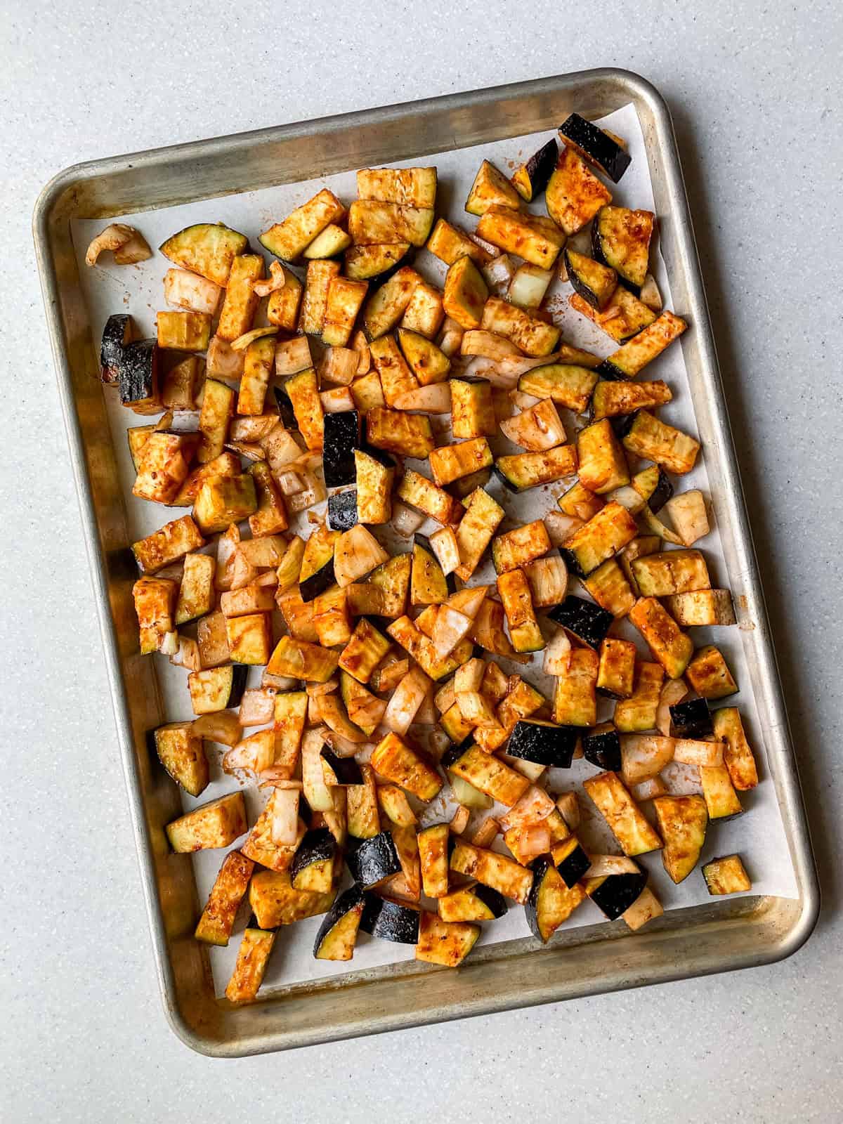 eggplant and onion spread out on parchment paper-lined sheet pan before baking