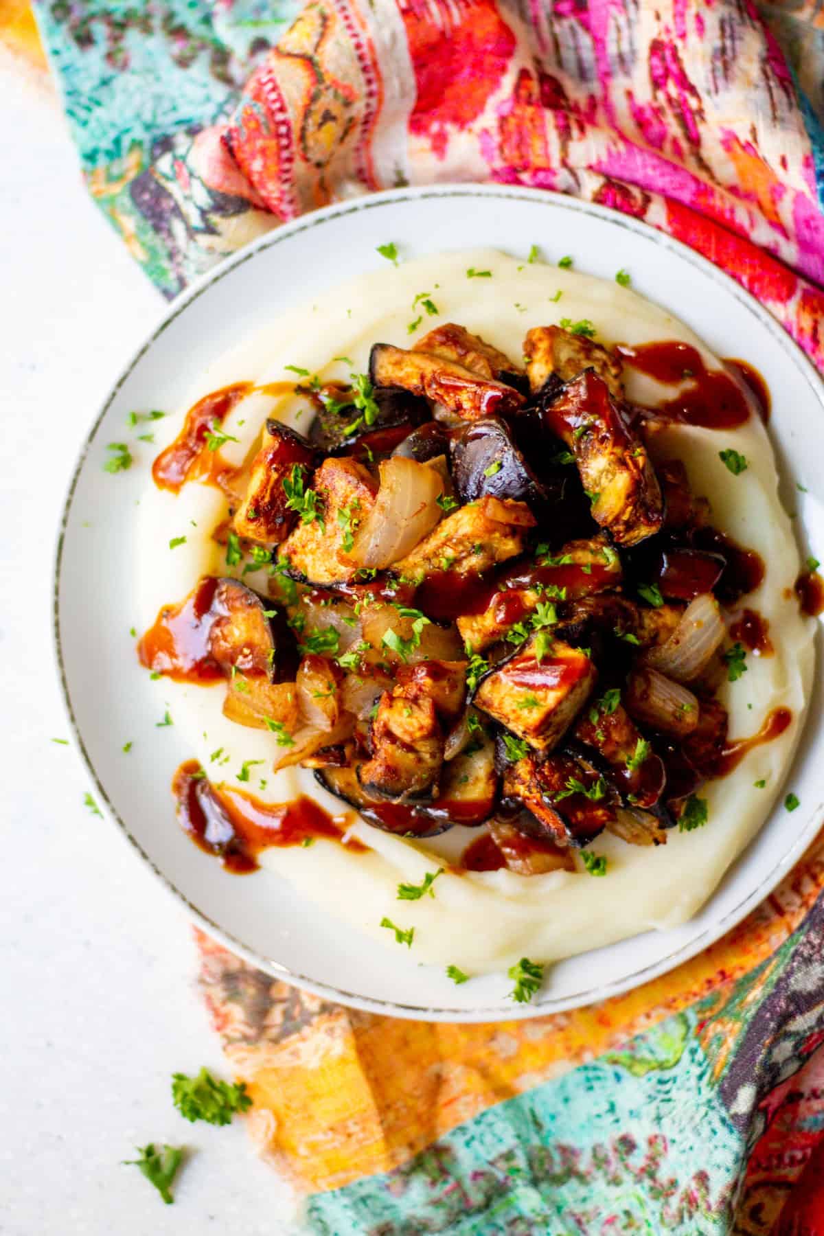 plate with roasted BBQ eggplant and onion on a bed of mashed potatoes with BBQ sauce drizzled on top