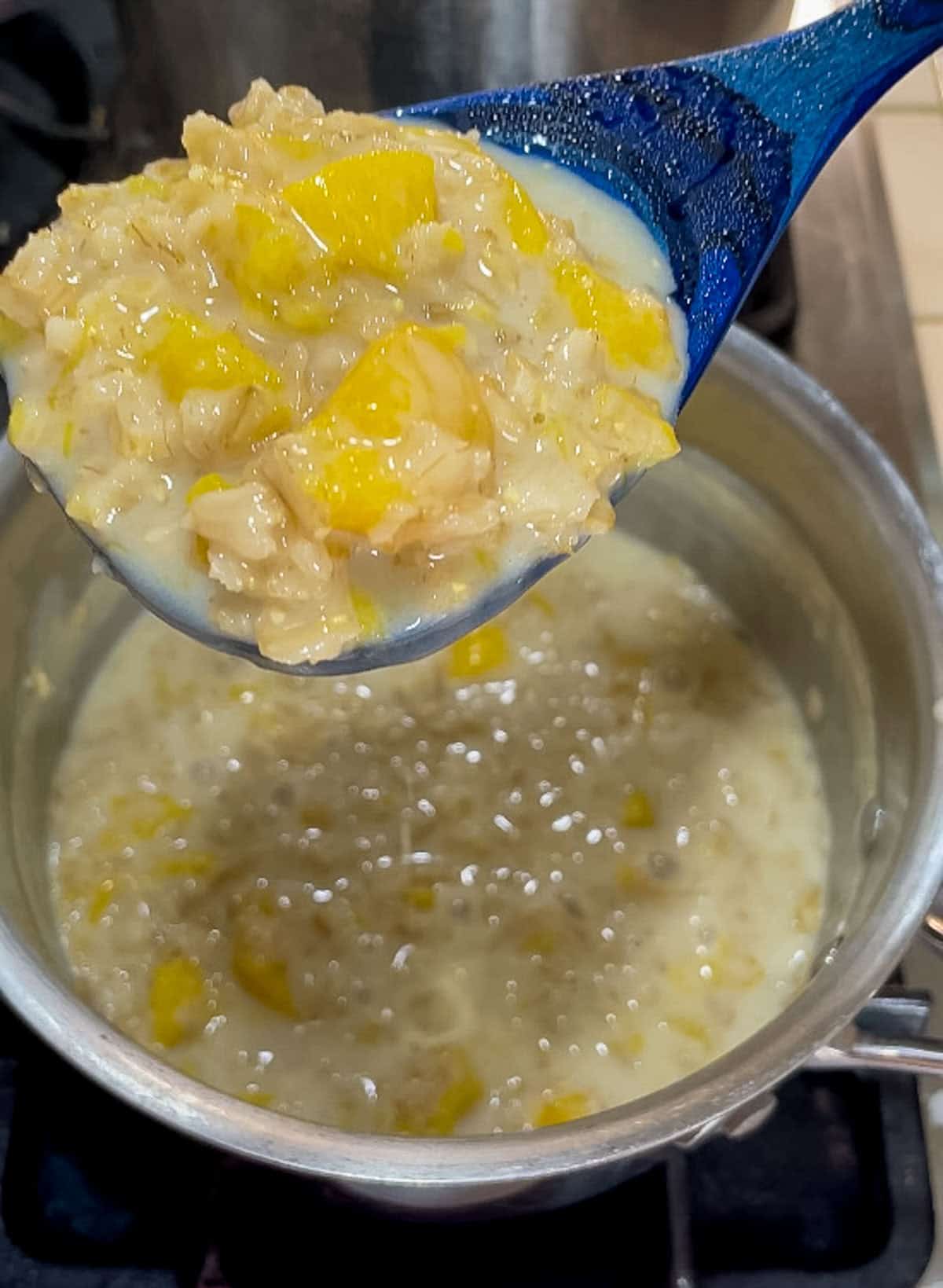 blue spoon full of cooked peaches and cream oatmeal from pan
