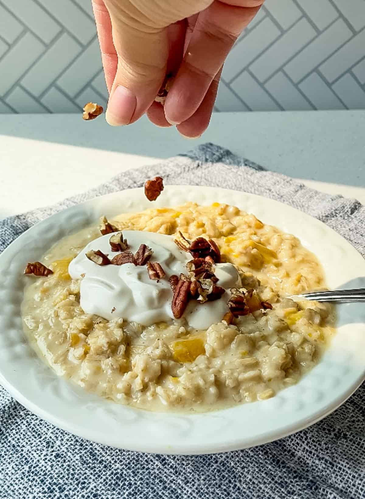 sprinkling chopped pecans over bowl of peaches and cream oatmeal with vanilla yogurt on top